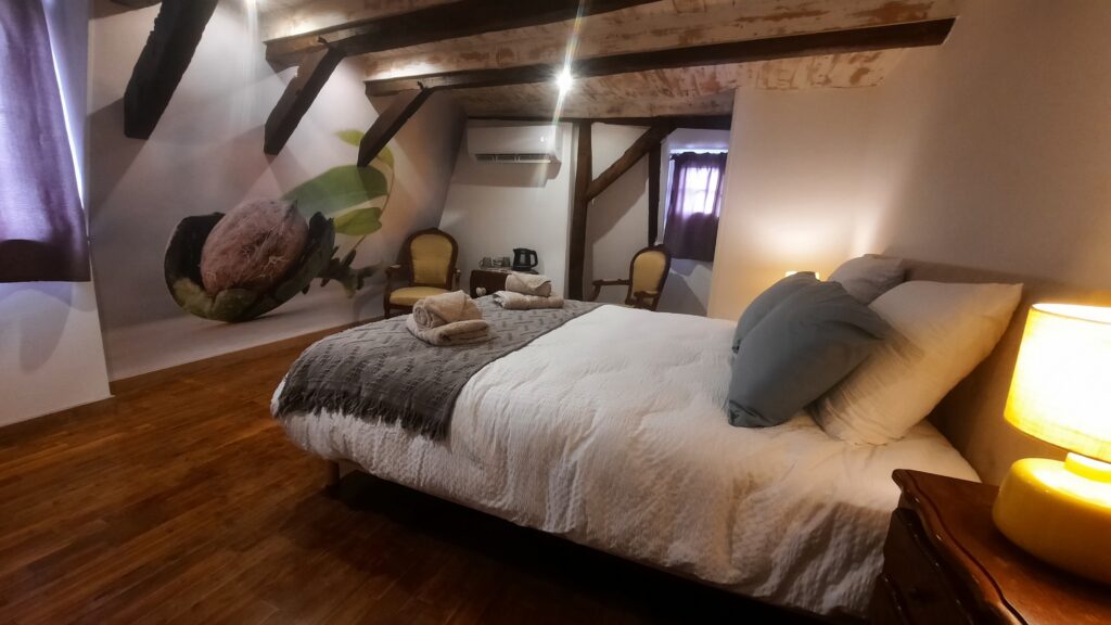 Vue du lit de la chambre Noix avec la tapisserie représentant une noix fraiche encore en partie dans sa gangue verte.